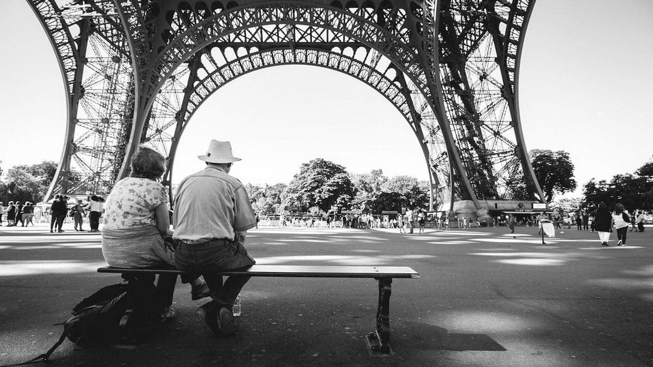 An elderly couple sitting on a bench under the Eiffel Tower, enjoying each other's company.