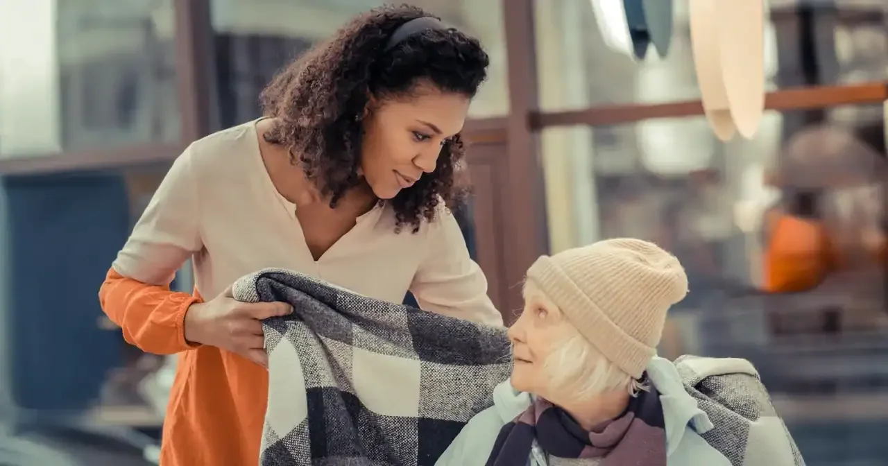 Young woman gently helping an elderly woman by wrapping a blanket around her shoulders