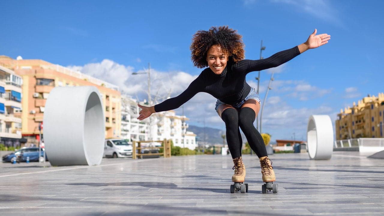 Smiling aesthetic skater wearing a black top and shorts cruising confidently on outdoor roller skates
