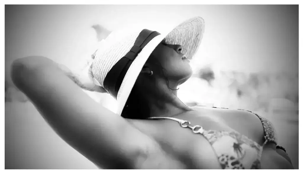 Black and white image of a woman reclining in a bikini and wide sun hat, face obscured.