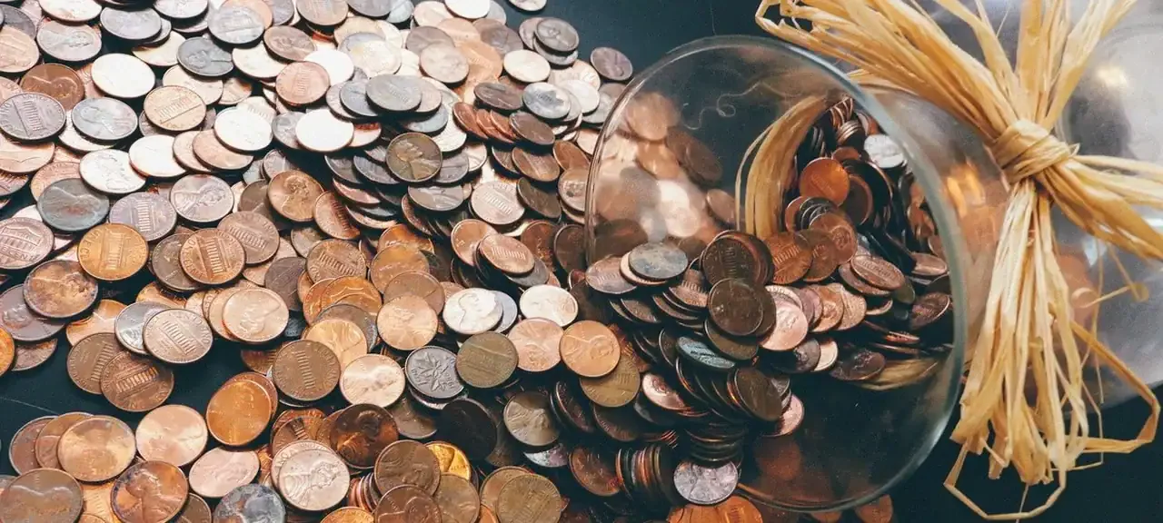 A glass jar spilling hundreds of pennies onto a surface