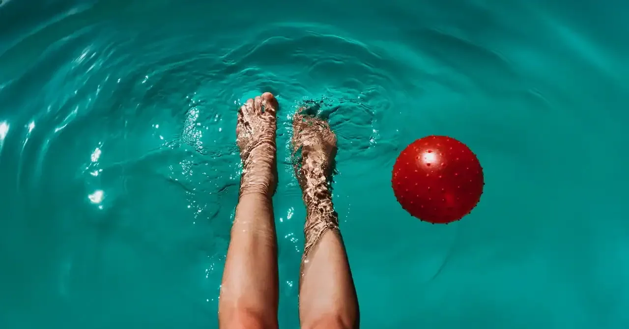 Woman's feet in a swimming pool with a red ball floating nearby