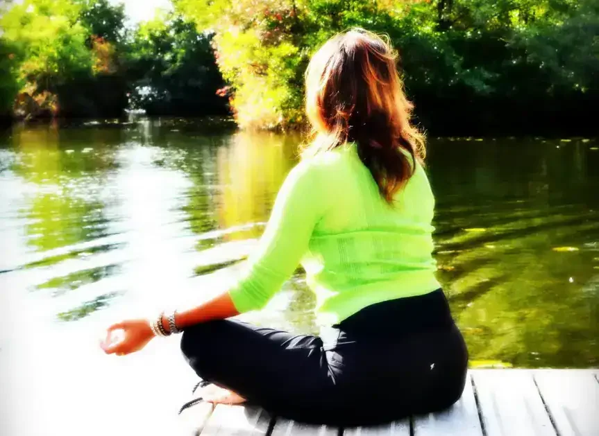 Woman in a green top meditating cross-legged by a calm lake