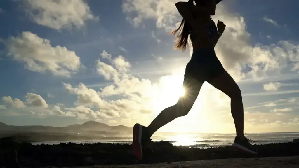Silhouette of a woman running alone along the coast at sunrise.