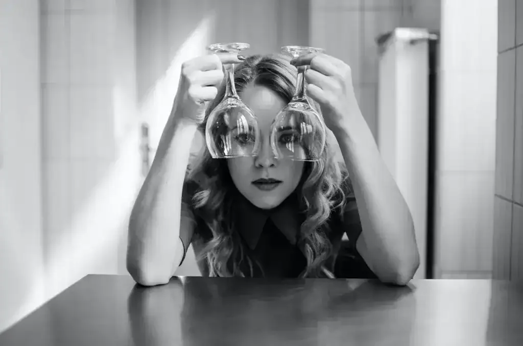 Woman holding two upside-down wine glasses over her eyes like lenses.